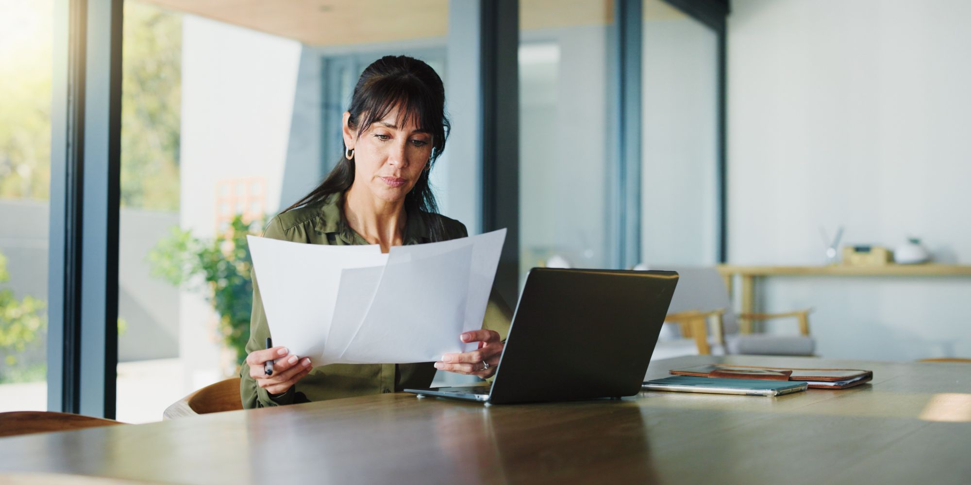 Frau am Tisch mit Laptop und Papieren